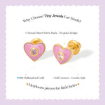 Tiny Jewels heart-shaped earrings with pink enamel and gold accents on a light purple background.