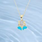 Gold pendant with turquoise accents and a diamond on a light blue water-like background  Tiny Jewels.