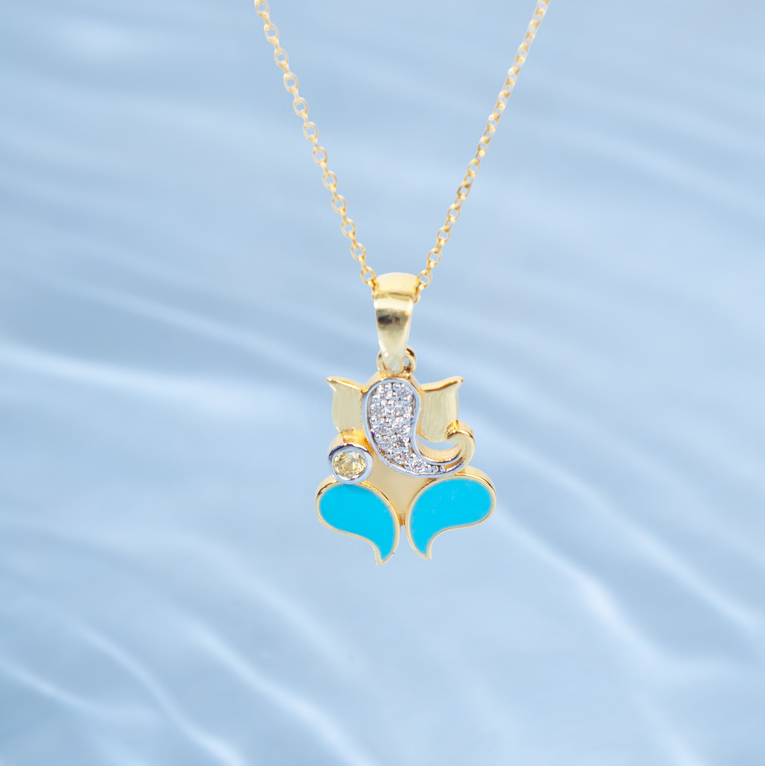 Gold pendant with turquoise accents and a diamond on a light blue water-like background  Tiny Jewels.