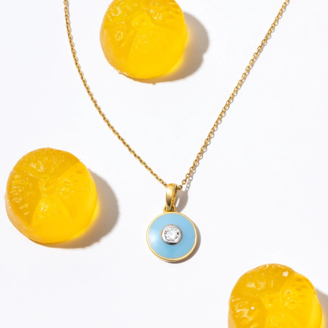 Gold necklace with a blue pendant featuring a diamond, surrounded by yellow circular objects on a white background Bubble_Pop_Pendant  Tiny Jewels.