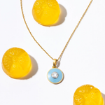 Gold necklace with a blue pendant featuring a diamond, surrounded by yellow circular objects on a white background Bubble_Pop_Pendant  Tiny Jewels.