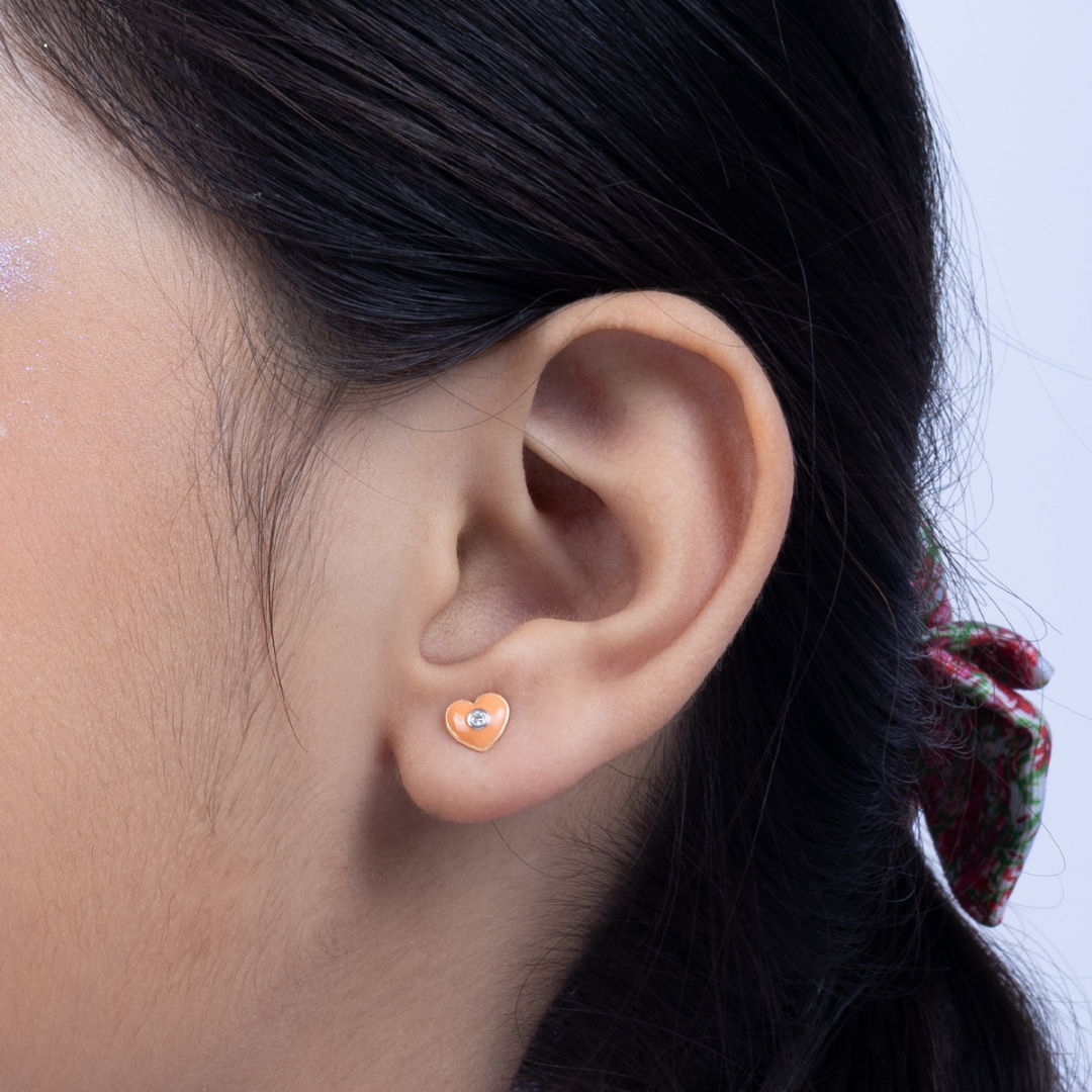 Tiny Jewels close-up of an ear wearing a heart-shaped earring with a blurred background