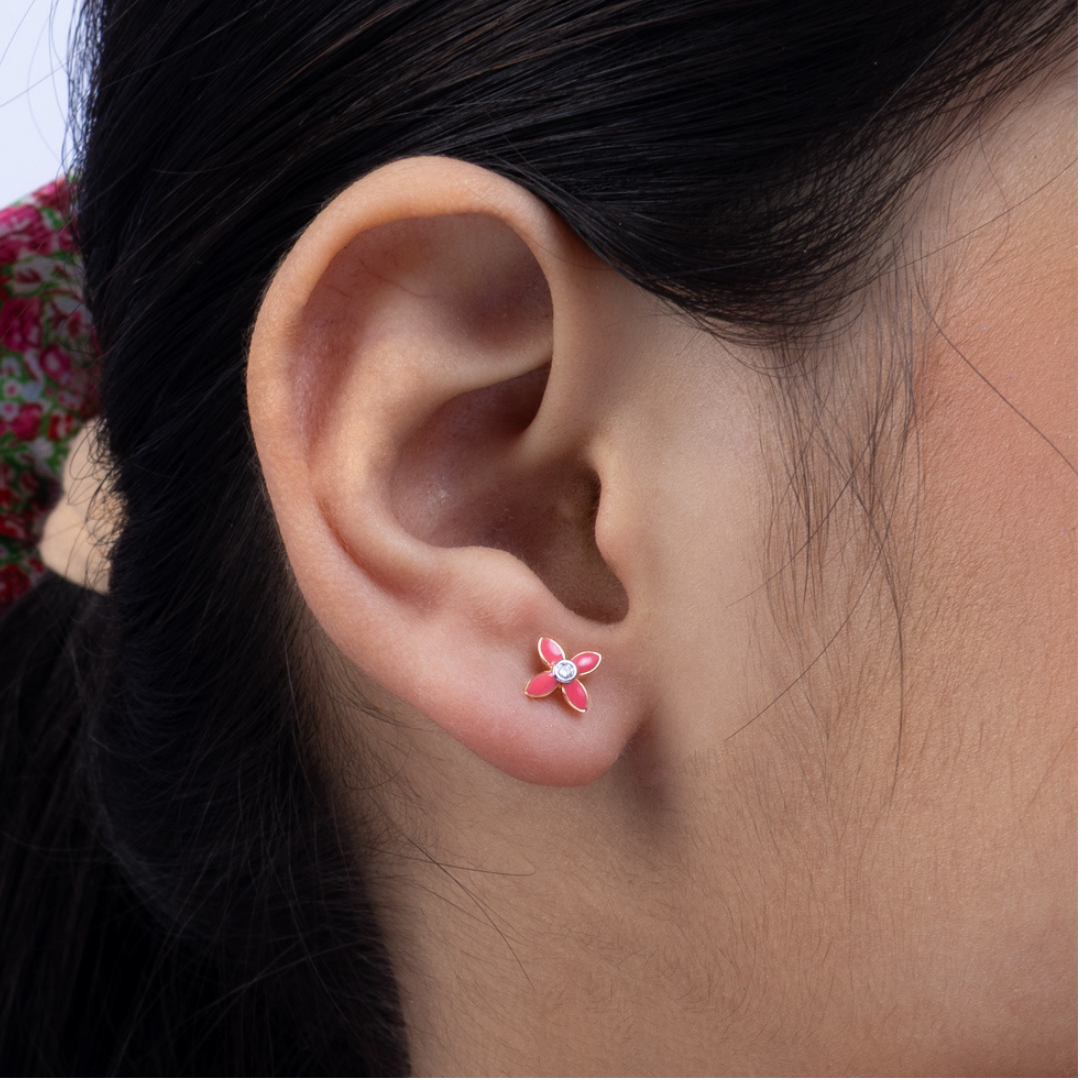 Tiny Jewels close-up of an ear wearing a pink flower-shaped earring with a clear gemstone.