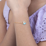 Tiny Jewels gold bracelet with a blue butterfly charm on a person wearing a purple outfit.