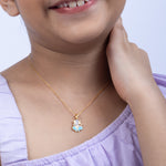 Child wearing a gold necklace with a blue pendant on a light purple background Tiny Jewels.