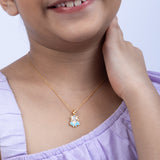 Child wearing a gold necklace with a blue pendant on a light purple background Tiny Jewels.