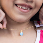 Close-up of a child wearing a gold necklace with a blue pendant  Tiny Jewels. Bubble_Pop_Pendant  Tiny Jewels.