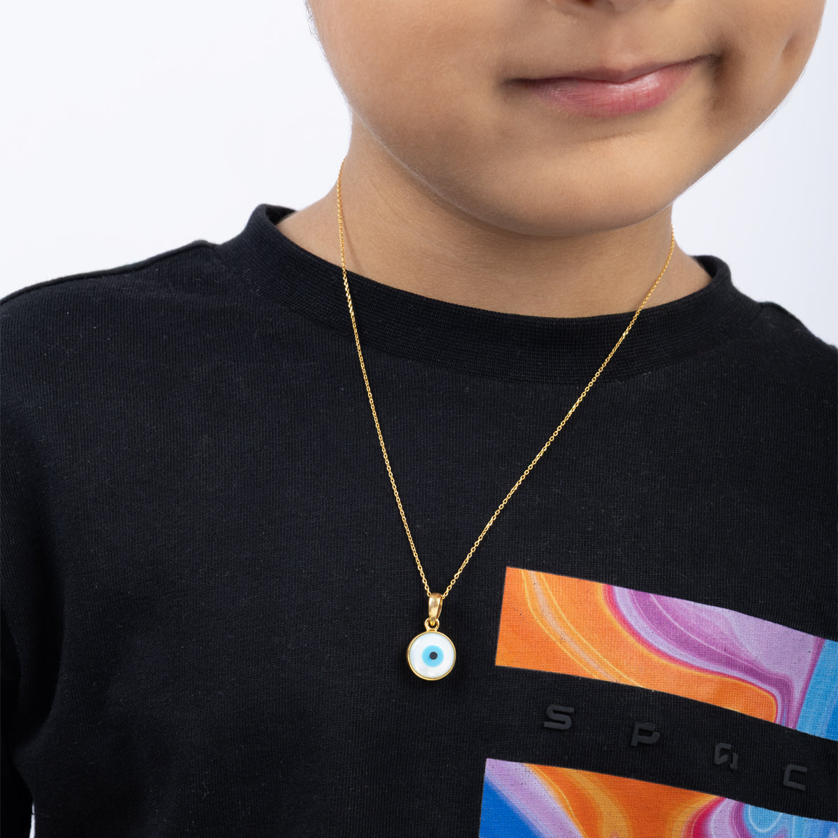 Tiny Jewels child wearing a gold necklace with an evil eye pendant on a black shirt with colorful design