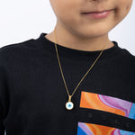 Tiny Jewels child wearing a gold necklace with an evil eye pendant on a black shirt with colorful design