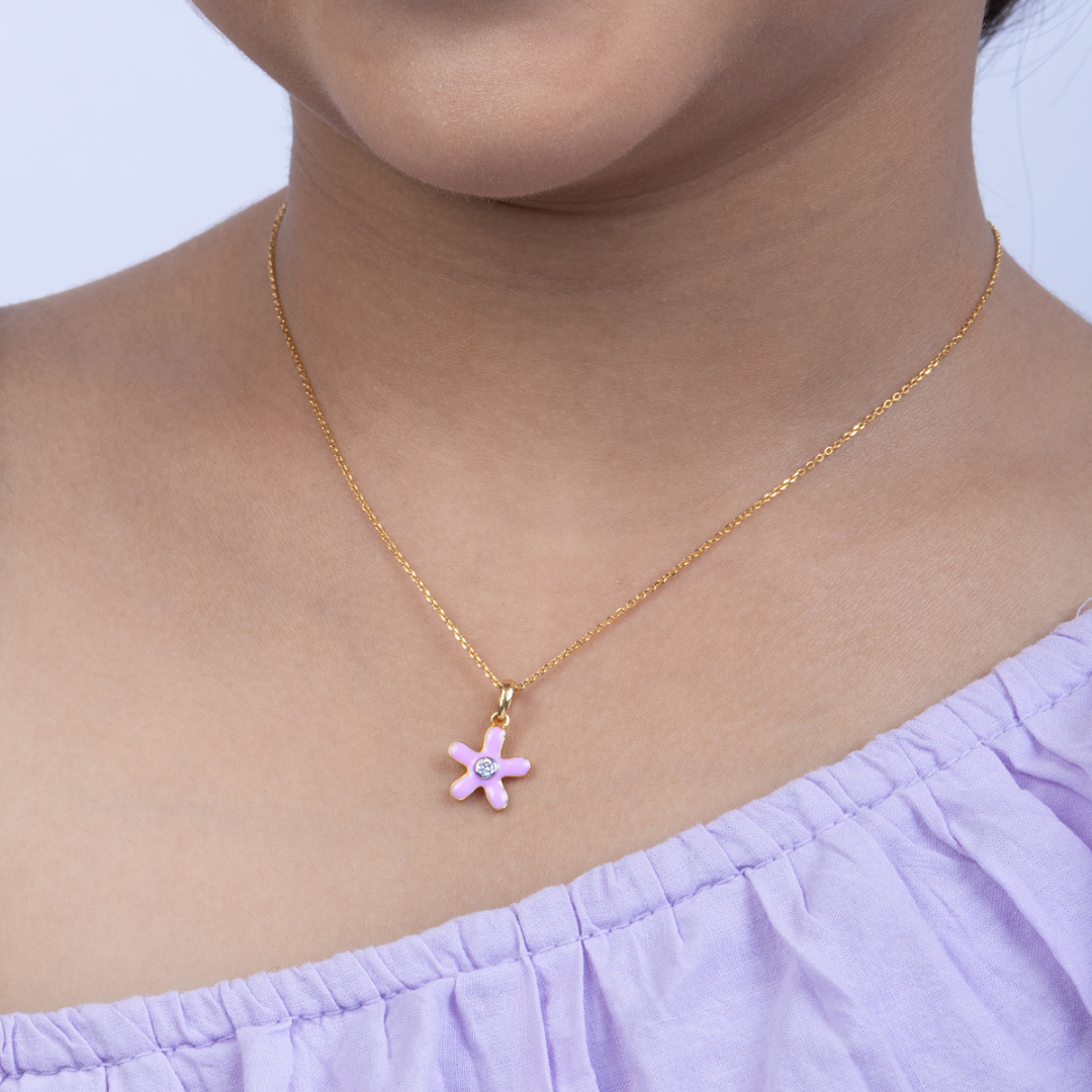 Tiny Jewels Gold necklace with a pink flower pendant worn by a person in a light purple top.