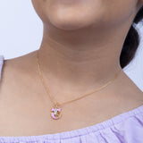 Gold necklace with a pink pendant worn by a person in a light purple top  Tiny Jewels.