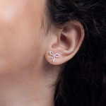 Tiny Jewels close-up of an ear wearing a bow-shaped earring with pink gemstones.