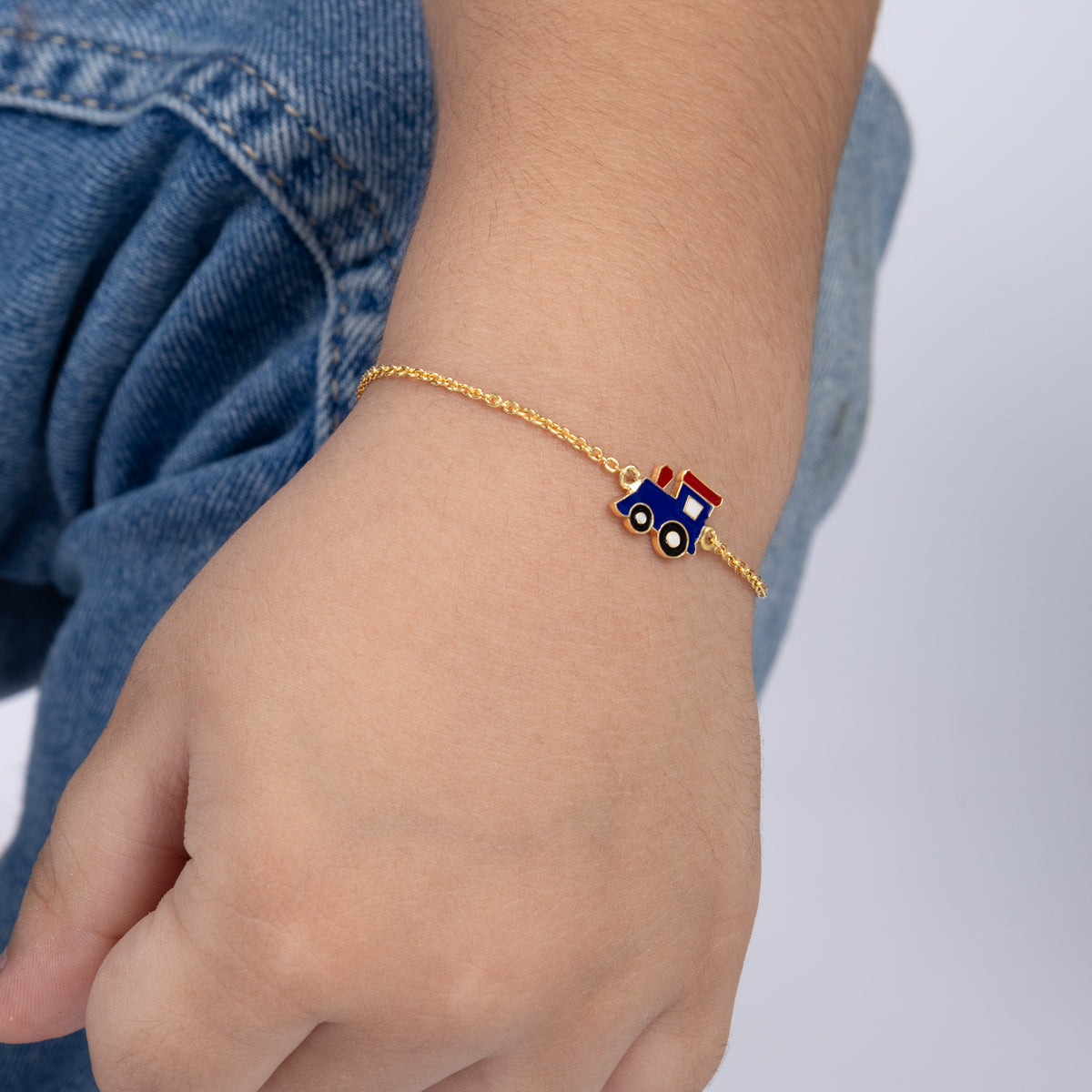 Tiny Jewels gold bracelet with a blue train charm on a child's wrist against a denim background