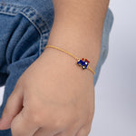 Tiny Jewels gold bracelet with a blue train charm on a child's wrist against a denim background