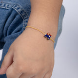 Tiny Jewels gold bracelet with a blue train charm on a child's wrist against a denim background