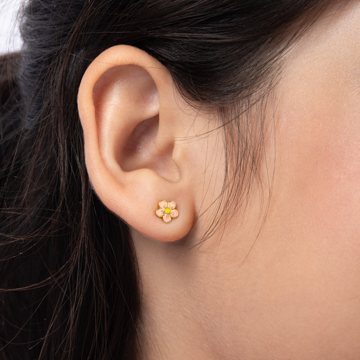 Tiny Jewels close-up of an ear wearing a floral earring with a yellow center.