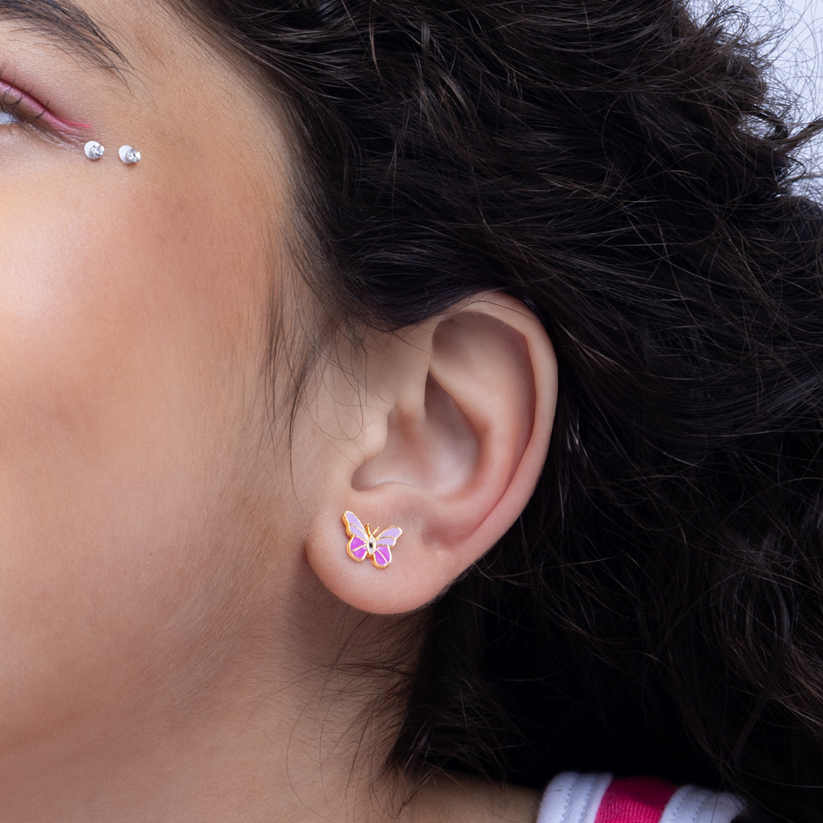 Tiny Jewels close-up of an ear wearing a butterfly-shaped earring with dark hair and visible makeup.