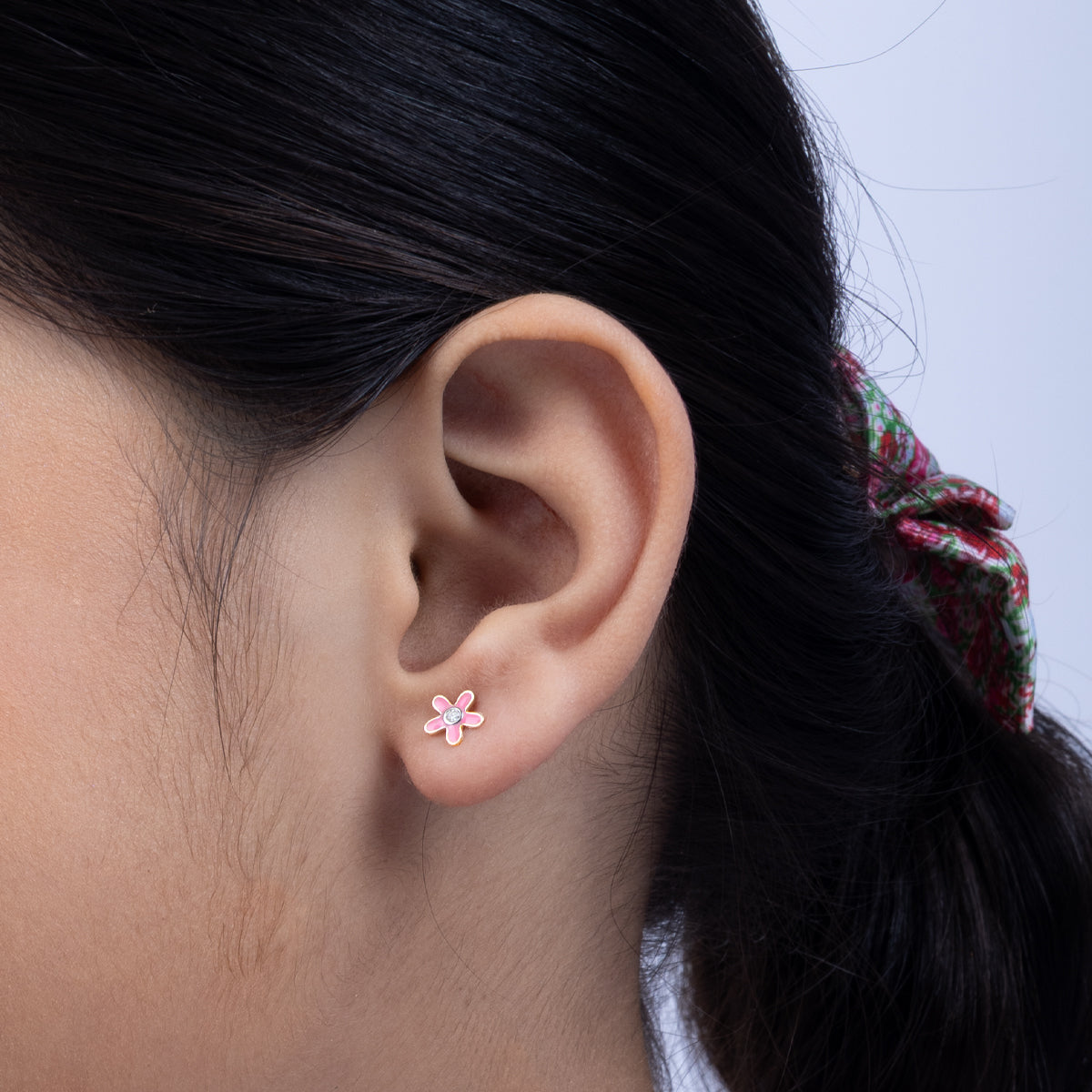 Tiny Jewels close-up of an ear wearing a pink flower earring with a blurred background