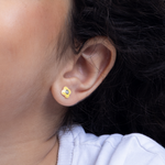 Tiny Jewels close-up of an ear wearing a yellow flower-shaped earring with a dark background