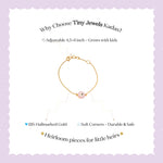 Tiny Jewels gold bracelet with a pink charm on a white background with promotional text about Tiny Jewels Kadas.