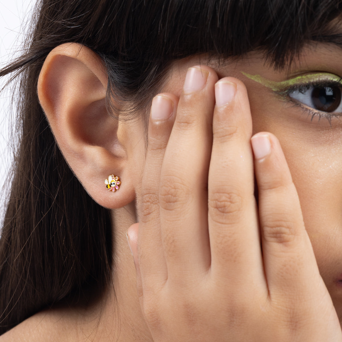 Tiny Jewels close-up of a person wearing colorful earrings with a hand covering part of their face.