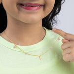 Tiny Jewels child wearing a gold necklace with pink beads, pointing to it.