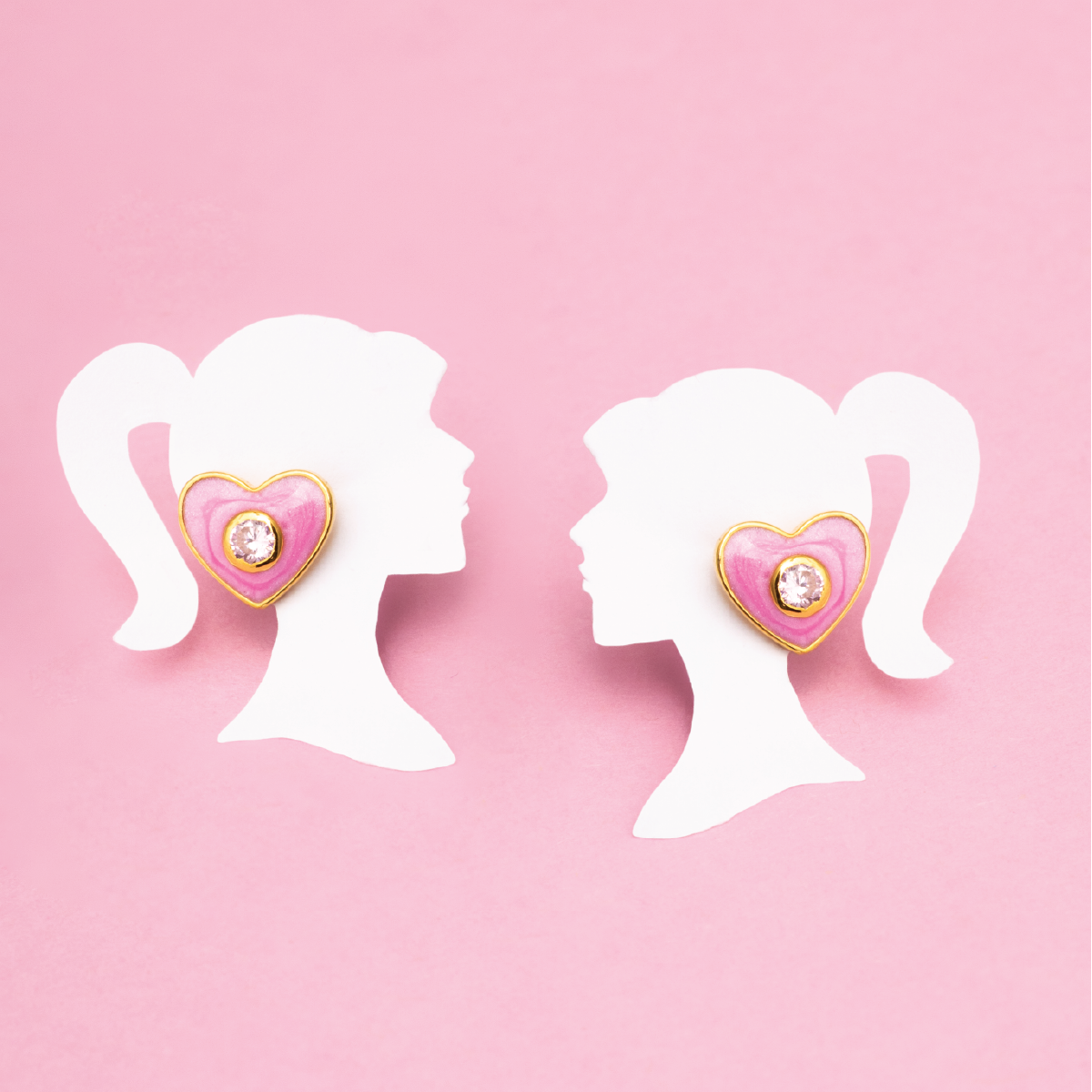 Tiny Jewels heart-shaped earrings on white silhouette mannequins against a pink background