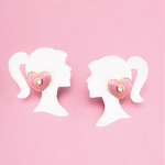 Tiny Jewels heart-shaped earrings on white silhouette mannequins against a pink background