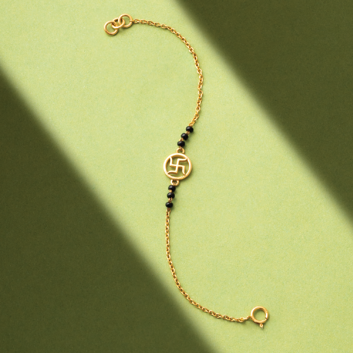 Tiny Jewels gold bracelet with black beads on a green background