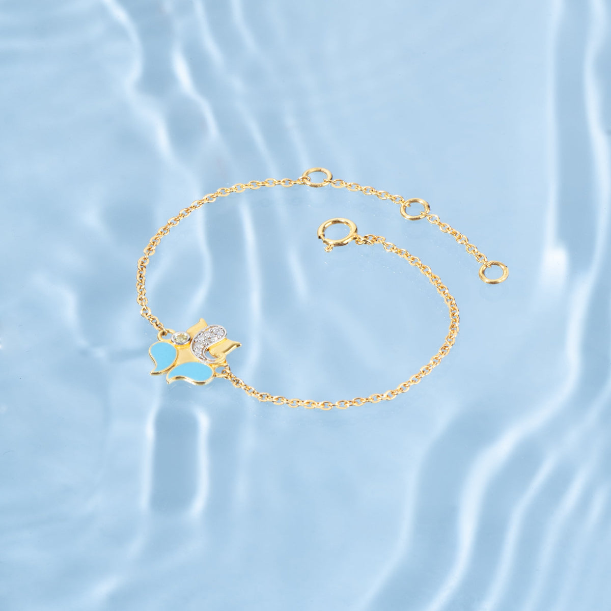 Tiny Jewels gold bracelet with a cat-shaped charm on a light blue water background