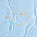 Tiny Jewels gold bracelet with a cat-shaped charm on a light blue water background