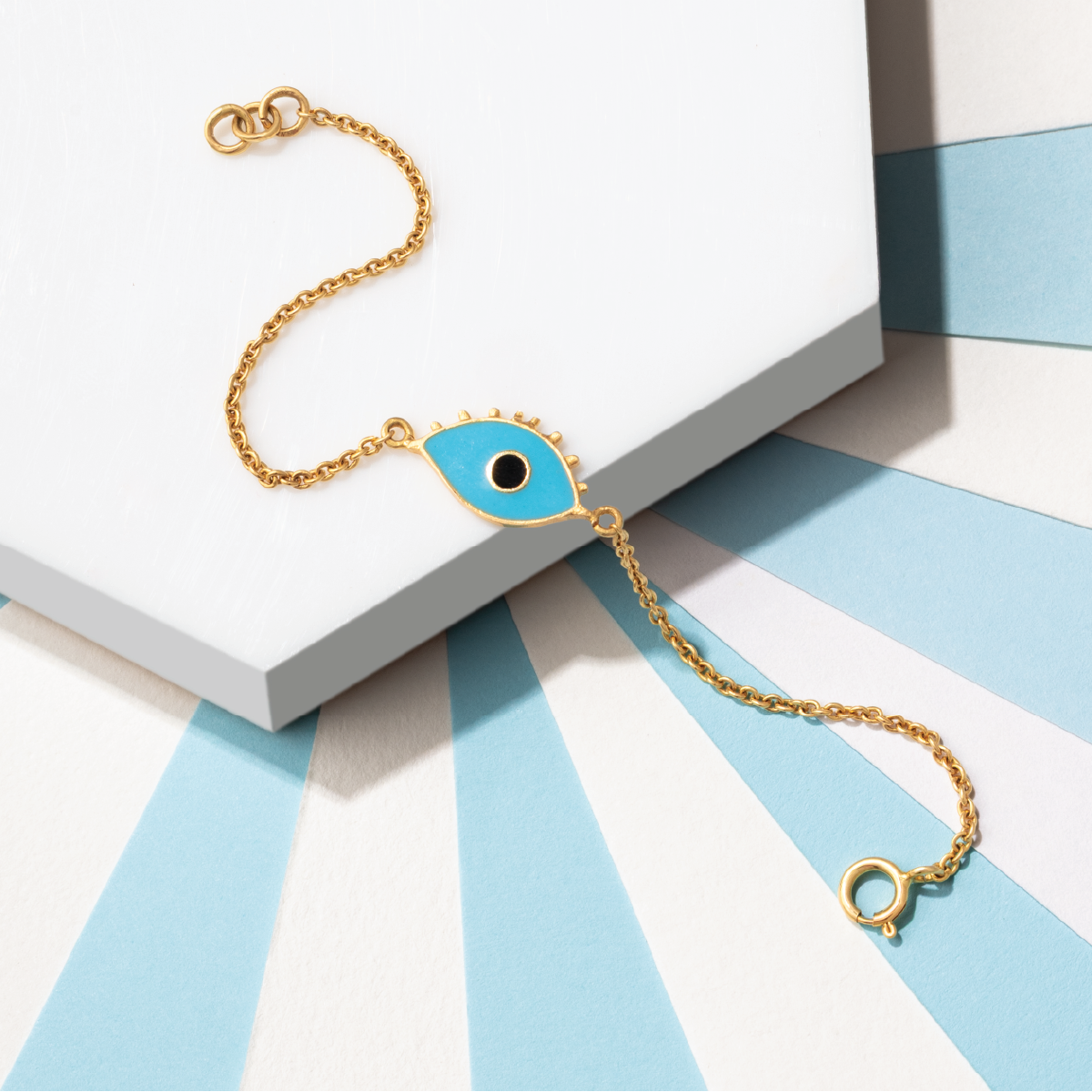 Tiny Jewels gold bracelet with a blue evil eye charm on a white and blue striped surface