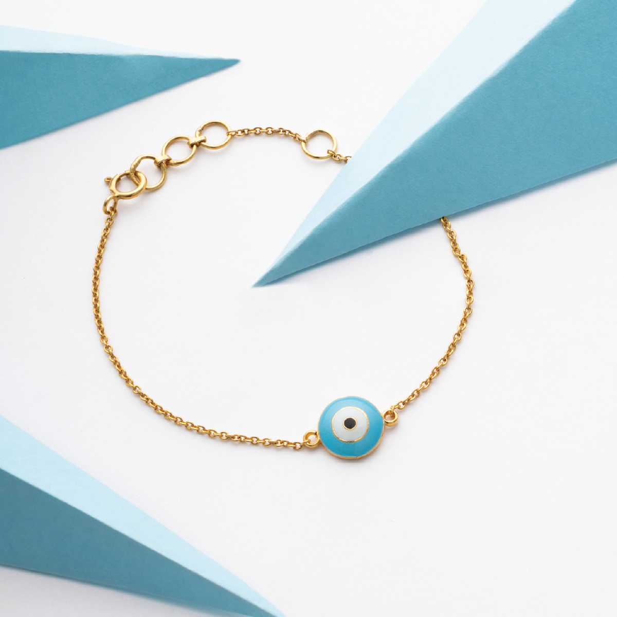 Tiny Jewels gold bracelet with a blue evil eye charm on a white and blue geometric background
