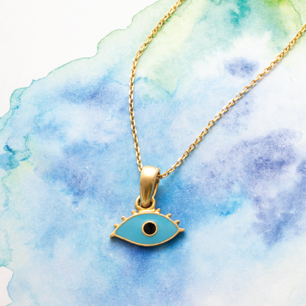 Tiny Jewels Gold necklace with a blue eye pendant on a watercolor background