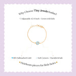 Tiny Jewels advertisement for Tiny Jewels Kadas bracelet with gold chain and blue evil eye charm on a light purple background.