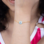 Tiny Jewels close-up of a gold bracelet with a blue gemstone on a person's wrist.