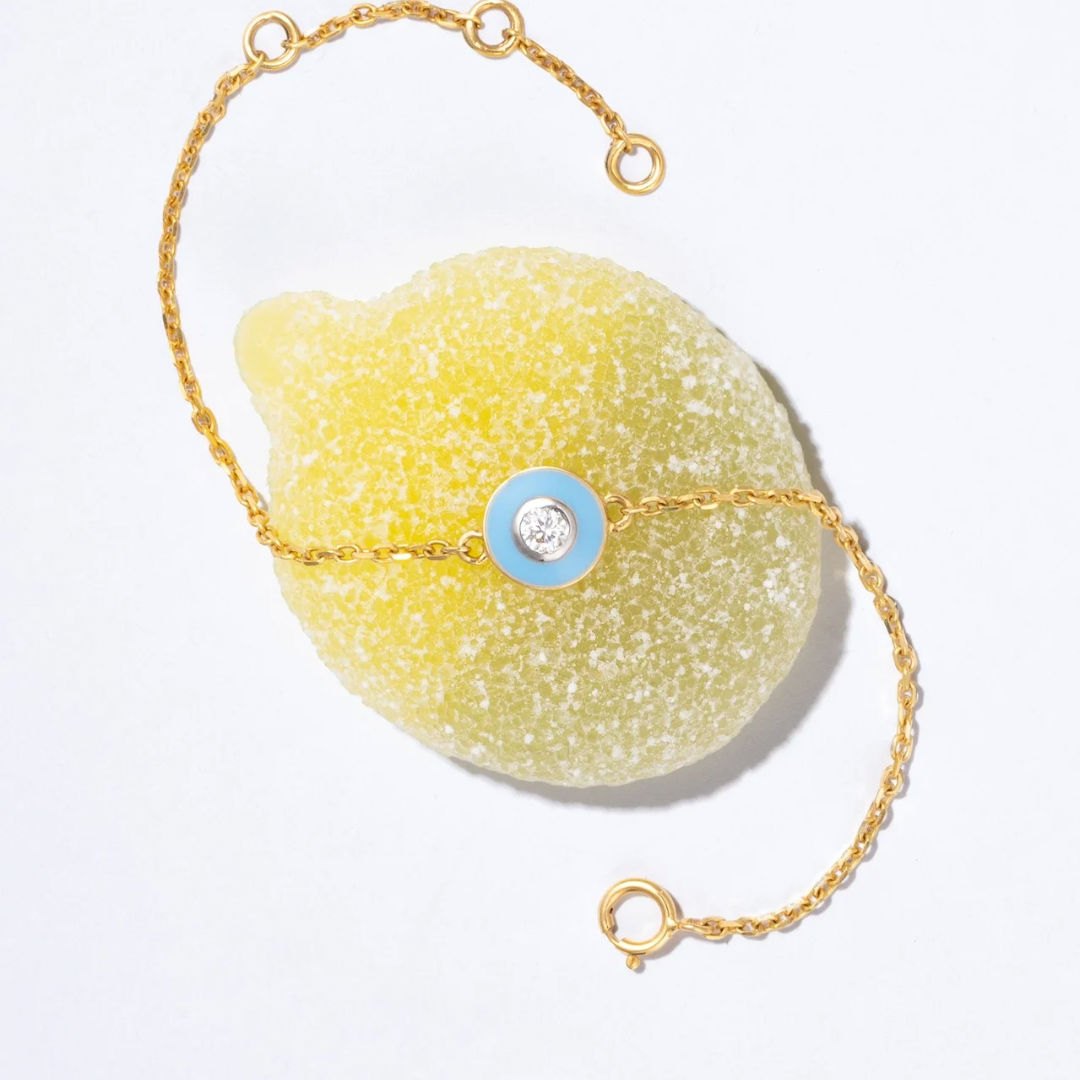 Tiny Jewels bracelet with a yellow stone and gold chain on a light gray background