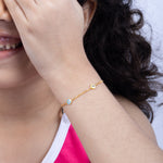 Tiny Jewels close-up of a child's arm wearing a gold bracelet with blue stones, against a neutral background.