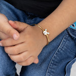 Tiny Jewels close-up of a child's hand wearing a gold bracelet with a white heart charm, against a denim background.