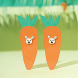 Tiny Jewels carrot-shaped earrings with bunny faces on a green and yellow gradient background