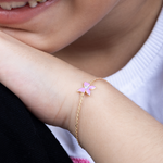 Tiny Jewels close-up of a person wearing a gold bracelet with a pink flower charm.