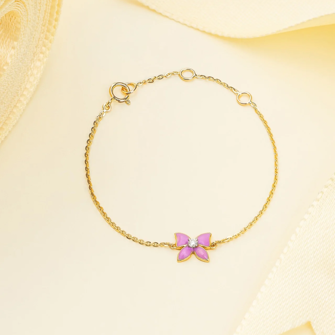 Tiny Jewels gold bracelet with a pink butterfly charm on a beige background