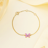 Tiny Jewels gold bracelet with a pink butterfly charm on a beige background