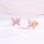 Tiny Jewels pink butterfly earrings with gold accents on a light pink background