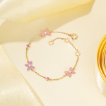 Tiny Jewels gold bracelet with pink floral charms on a yellow satin background