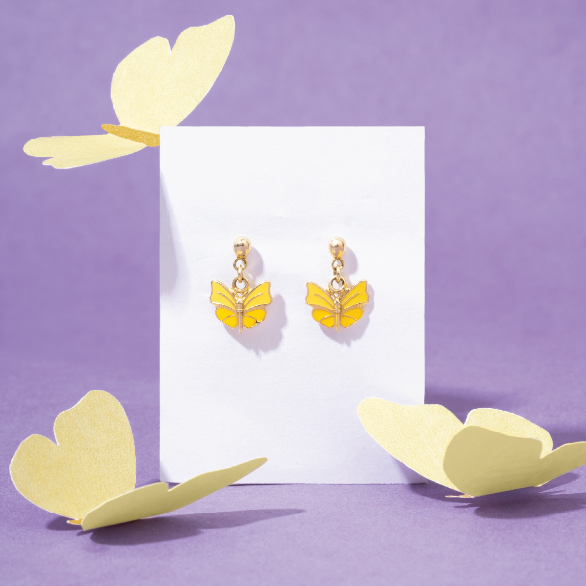 Tiny Jewels yellow butterfly earrings on a white card with decorative yellow leaves on a purple background