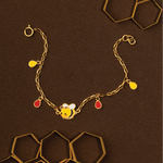 Tiny Jewels gold bracelet with a bee charm on a brown background