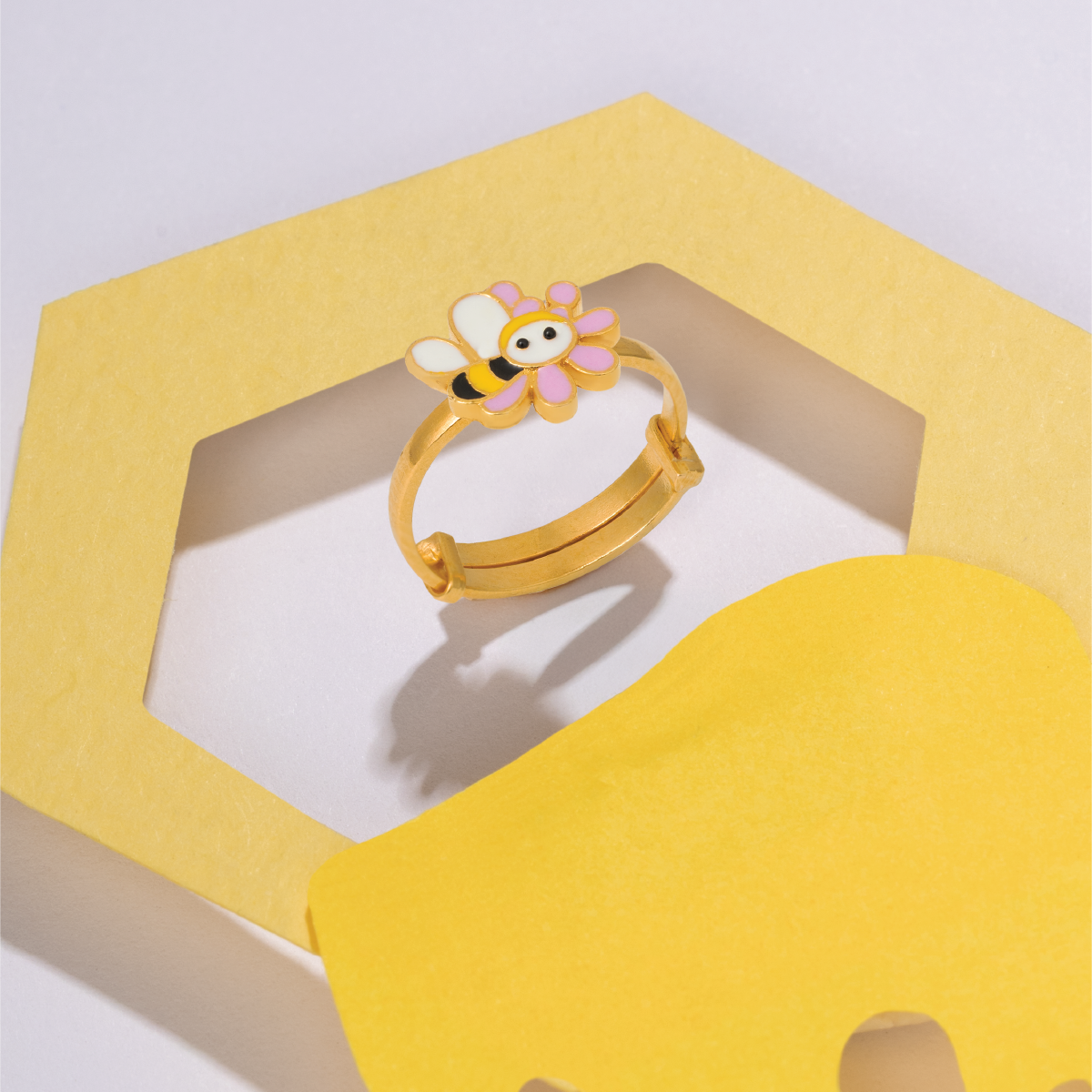 Tiny Jewels gold ring with a colorful bee design on a yellow elephant-shaped stand.