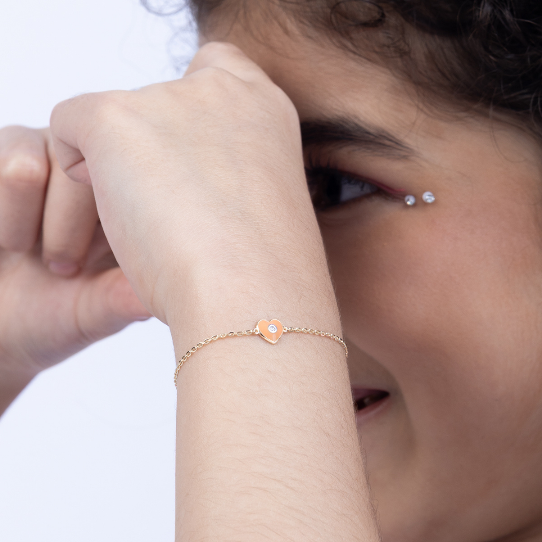 Tiny Jewels close-up of a person wearing a gold bracelet with a heart-shaped charm.