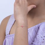 Tiny Jewels person wearing a delicate gold bracelet with a pink heart charm on a light purple top.
